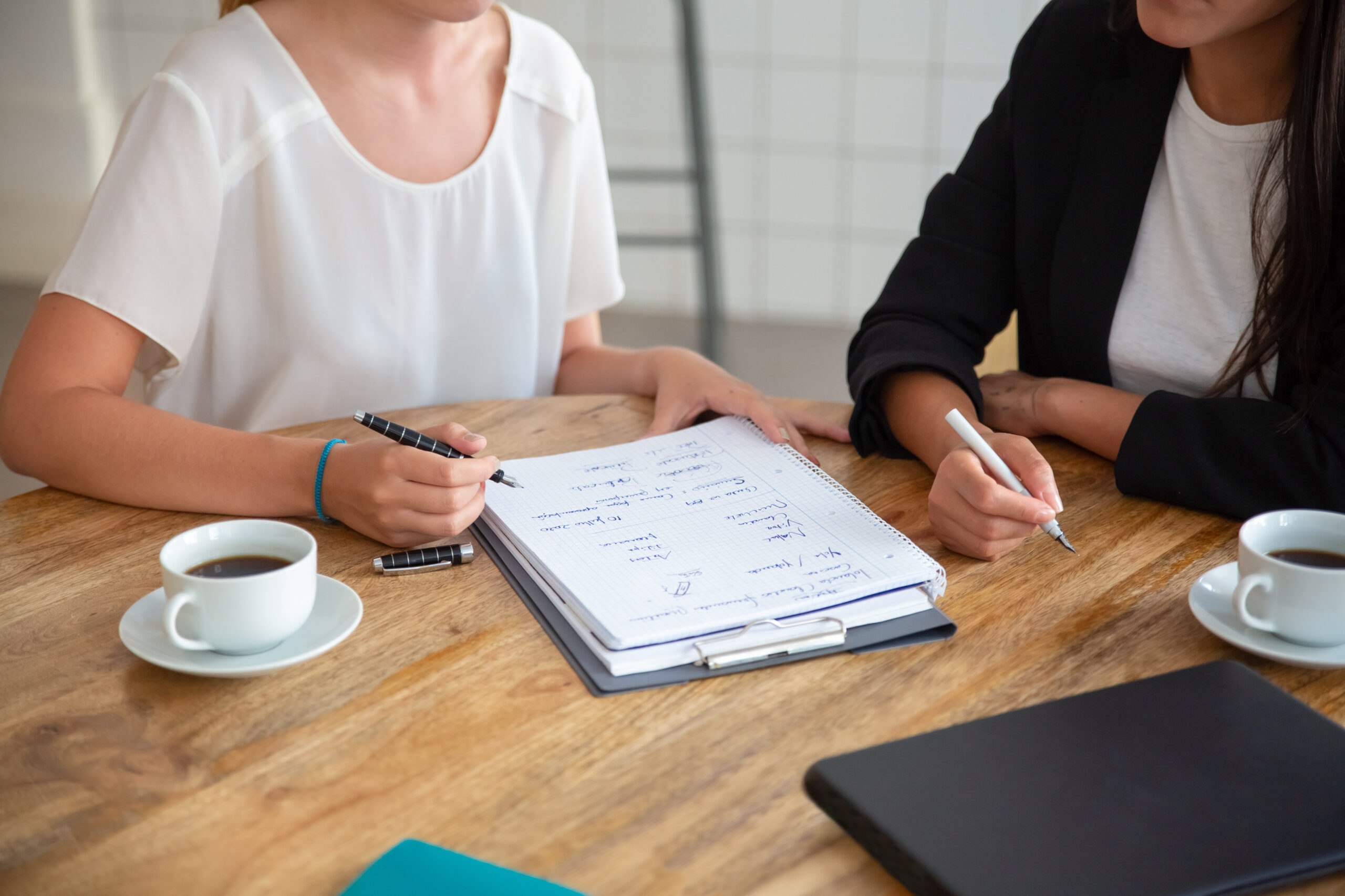 Young female colleagues meeting and discussing business plan, writing strategy scheme on paper, making draft. Cropped shot. Planning concept